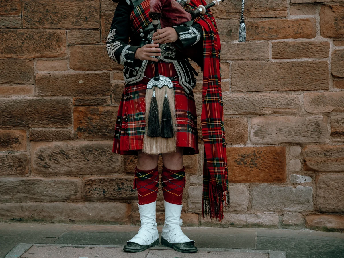 Close detail of a piper's kilt, sporran and bagpipe chanter against a stone wall